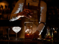 Bartender stirring a cocktail in the measuring glass cup on the bar counter in the dark blurred background