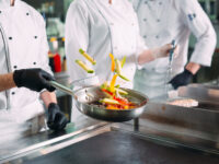 Chefs in protective masks and gloves prepare food in the kitchen of a restaurant or hotel